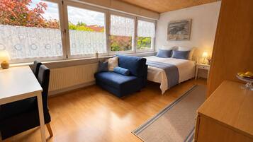 Ein kompaktes Zimmer mit Bett, einer kleinen Sitzecke, einem Tisch und Blick nach draußen.