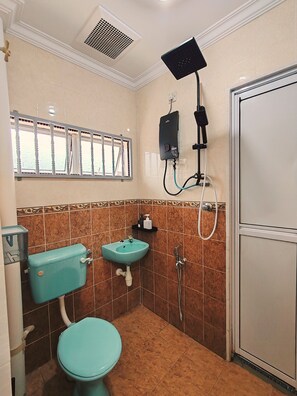 Une salle de bain comprenant des toilettes, un lavabo, une douche et une fenêtre ornée d’une grille décorative.
