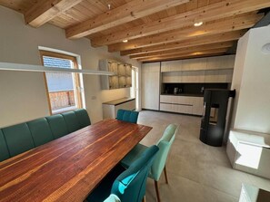 Een moderne keuken met houten balken in het plafond, een eethoek met een houten tafel en teal stoelen, en een ingebouwde bank.
