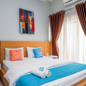 Una habitación de hotel con una cama, almohadas, una manta azul, una toalla y un cuadro en la pared.