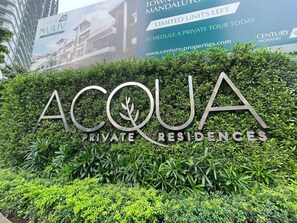 Een bordje voor 'ACQUA PRIVATE RESIDENCES' met een haag op de voorgrond.