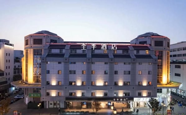 Un hôtel à plusieurs étages, doté d’une architecture moderne, se caractérise par une façade symétrique avec des fenêtres régulièrement espacées et une entrée centrale.