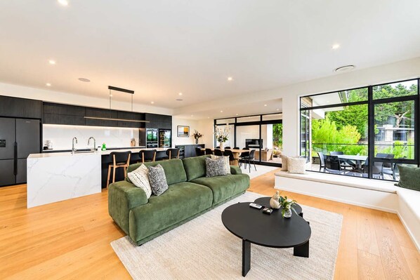 A modern kitchen with dark cabinetry, a marble countertop, and a dining area with a green sofa and a round coffee table.