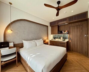 A hotel room with a bed, a desk, a chair, a vanity with a mirror, and a ceiling fan. - Hans Signature Hotel  (Hai Chau)