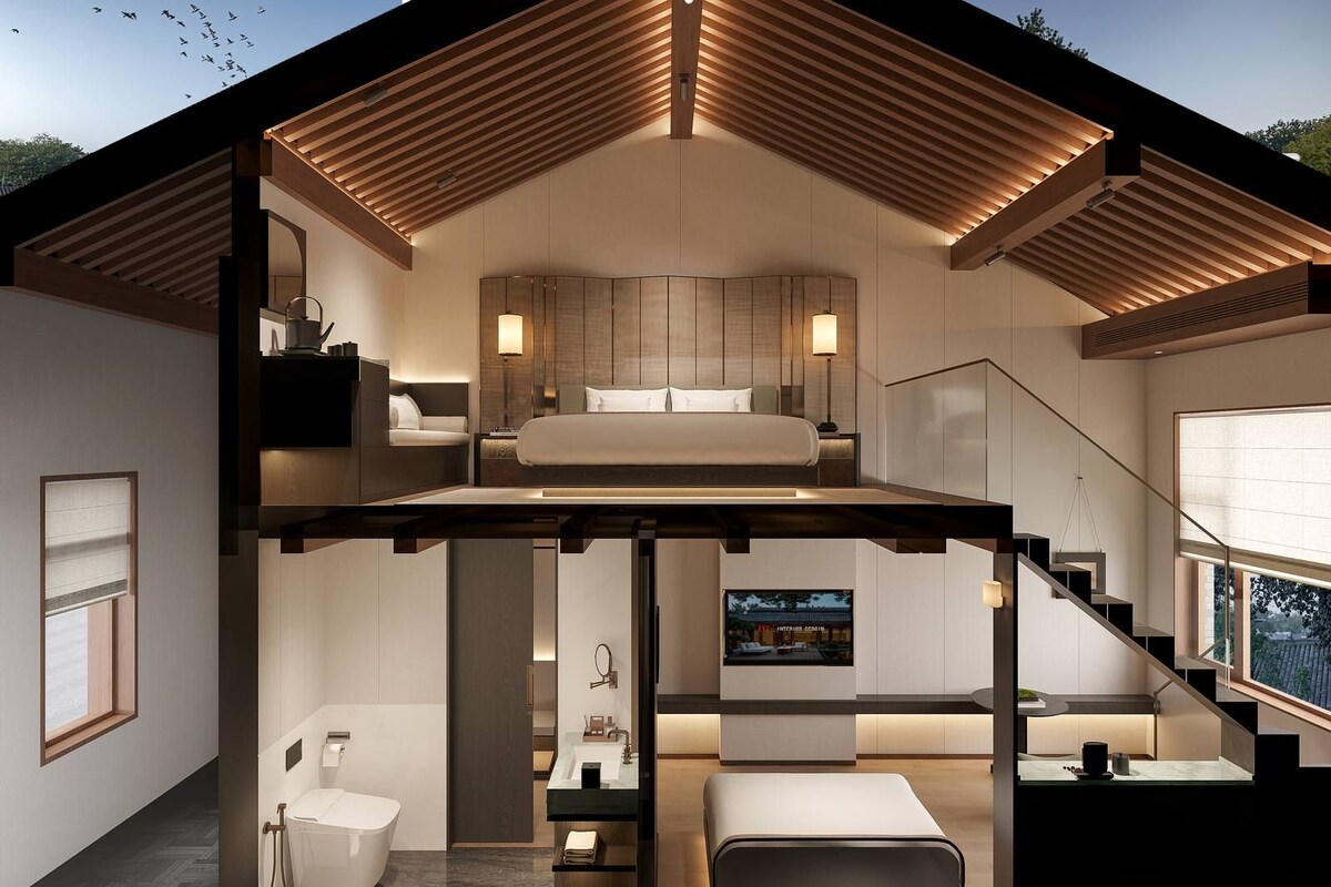 Una habitación de hotel moderna con cama altillo, zona de estar, baño y un ventanal grande.