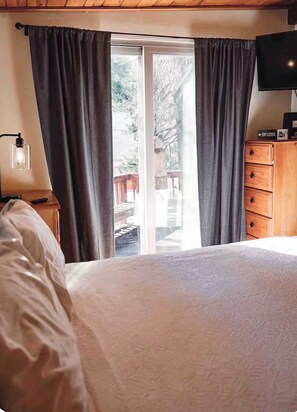 Een slaapkamer met een bed, een houten dressoir, een televisie en een schuifpui die leidt naar een buitenruimte.