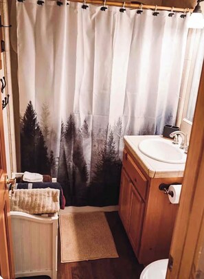 Een badkamer met een douchegordijn met een natuurprint, een wastafel en houten kastjes.