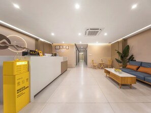 Un espace d’accueil d’hôtel comprenant un comptoir de réception, un coin salon et une plante.