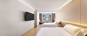 Une chambre d’hôtel dotée d’un téléviseur à écran plat fixé au mur, de deux lits avec du linge de lit blanc, d’une petite table ronde et offrant une vue sur la ville grâce à de grandes fenêtres.