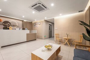 Un espace d’accueil moderne comprenant un comptoir de réception, une table basse avec un bol de collations et deux chaises en bois.