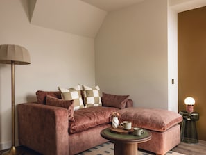 Ein gemütliches Wohnzimmer mit einem braunen Sofa, einer Stehlampe und einem Beistelltisch mit Lampe.
