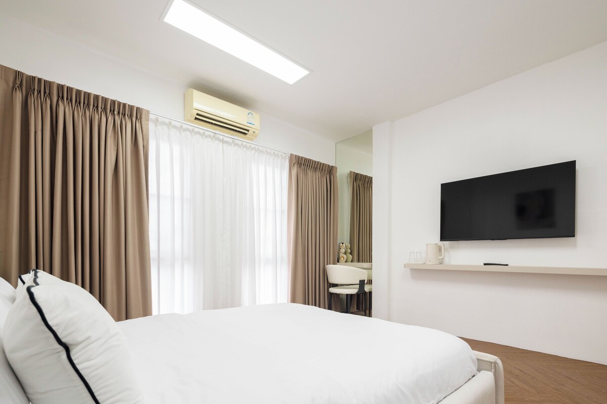 A modern hotel room with a large bed, a flat-screen TV, a bedside table, and a window with curtains.