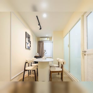 A modern dining area with a round table and four chairs, a ceiling light, and a view through a glass door. - Arunvara Stay (Ratchathewi)