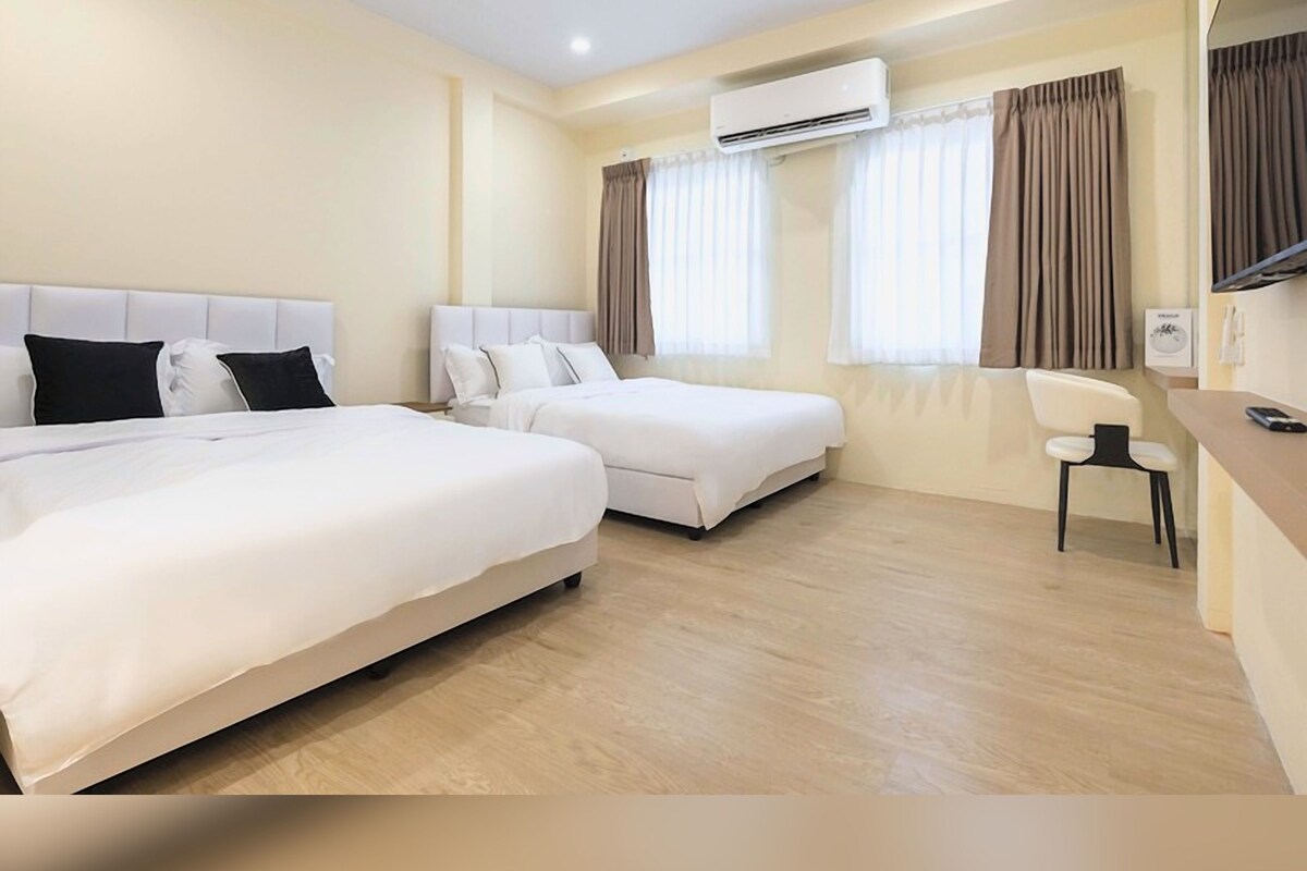 A hotel room with two beds, a desk, a chair, an air conditioning unit, and curtains.