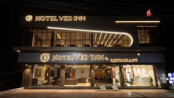 A hotel with a modern facade, a prominent sign for the hotel and restaurant, and a well-lit entrance.