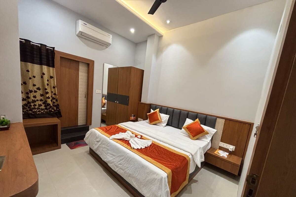 A hotel room with two beds, a wooden wardrobe, a desk, and a bathroom with a shower curtain.