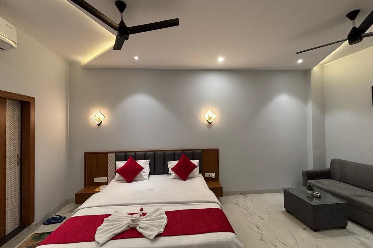 A modern bedroom with a bed, bedside tables, a sofa, and ceiling fans.