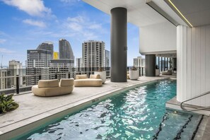 A rooftop pool area with seating and a city skyline view. - Luxury 60th Floor | Panoramic Gold Coast Views | 2BR (Broadbeach)