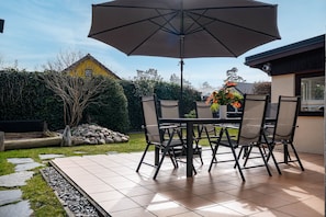 Eine Terrassengruppe im Freien mit Tisch, Stühlen, einem großen Sonnenschirm und einer Blumenkomposition.