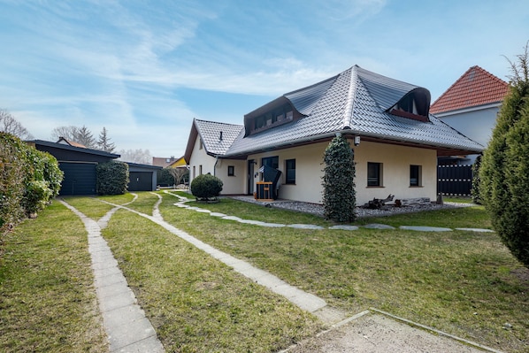 Ein Wohnhaus mit geneigtem Dach, einer Veranda und einem Weg zum Eingang.