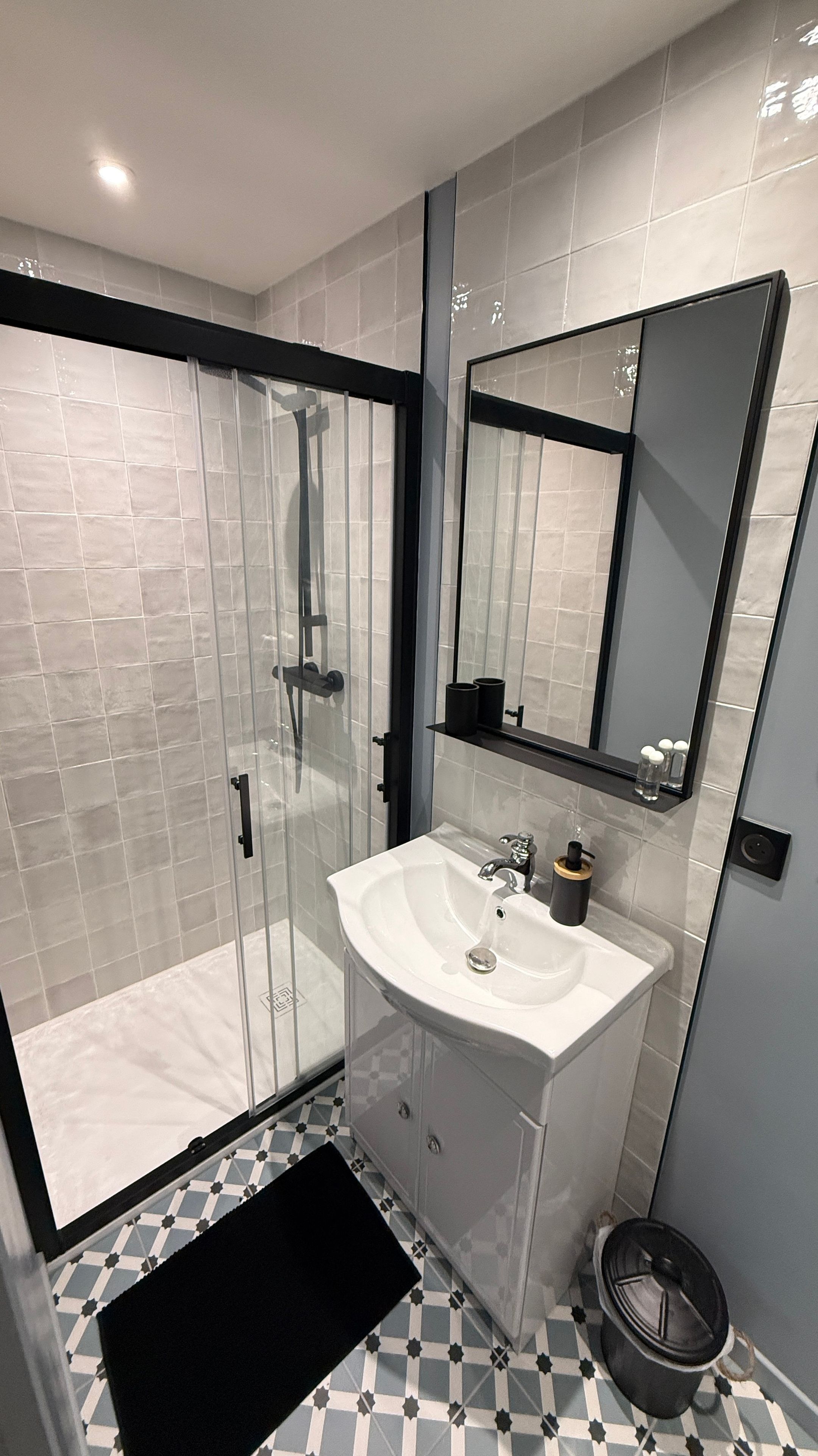 Ein modernes Badezimmer mit einer Duschkabine aus Glas, einem weißen Waschbecken mit Spiegel darüber und einem gestreiften Boden.