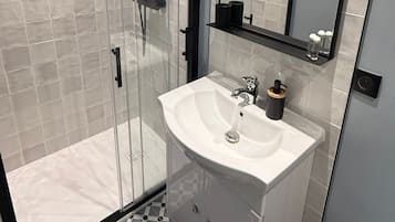 Ein modernes Badezimmer mit einer Duschkabine aus Glas, einem weißen Waschbecken mit Spiegel darüber und einem gestreiften Boden.