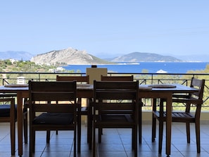 Una mesa y sillas de madera en un balcón con vistas al mar y a las montañas.