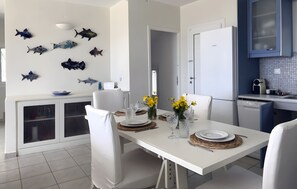 Una cocina moderna con armarios blancos, una mesa de comedor para cuatro personas y decoración de peces en la pared.