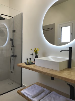Un baño moderno con cabina de ducha acristalada, un lavabo blanco con grifo negro y un espejo redondo con marco iluminado.