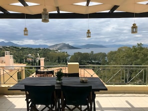 Una terraza con mesa y sillas, con vistas a un paisaje montañoso y una masa de agua.