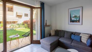 A modern living room with a grey sofa, a small round table, and a view of a garden through a sliding glass door.