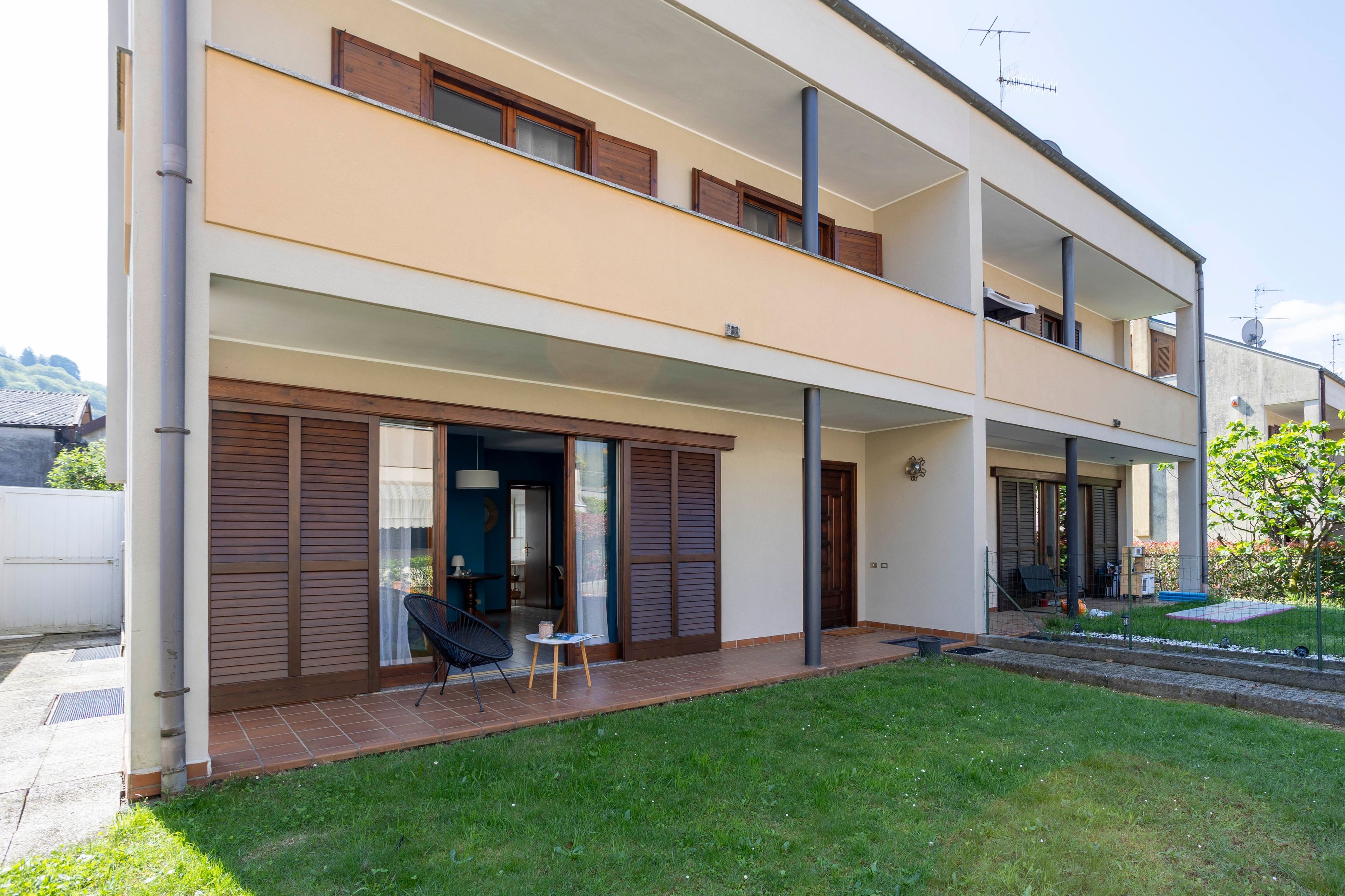 A two-story residential building with a balcony, a sliding glass door entrance, and a small outdoor seating area.