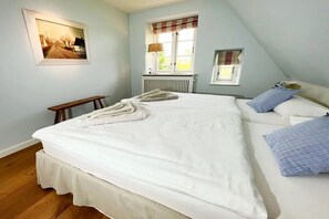 A bedroom with a large bed, a bedside table, a window with curtains, and a radiator.