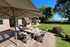 An outdoor patio with a table and chairs, a covered area, and a view of a grassy field.