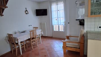 Une pièce comprenant une table à manger, des chaises, un téléviseur, une fenêtre avec des rideaux et un coin cuisine avec un plan de travail.