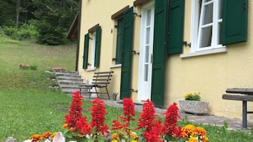 A yellow building with green shutters, a bench, and a flower bed with red and orange flowers.