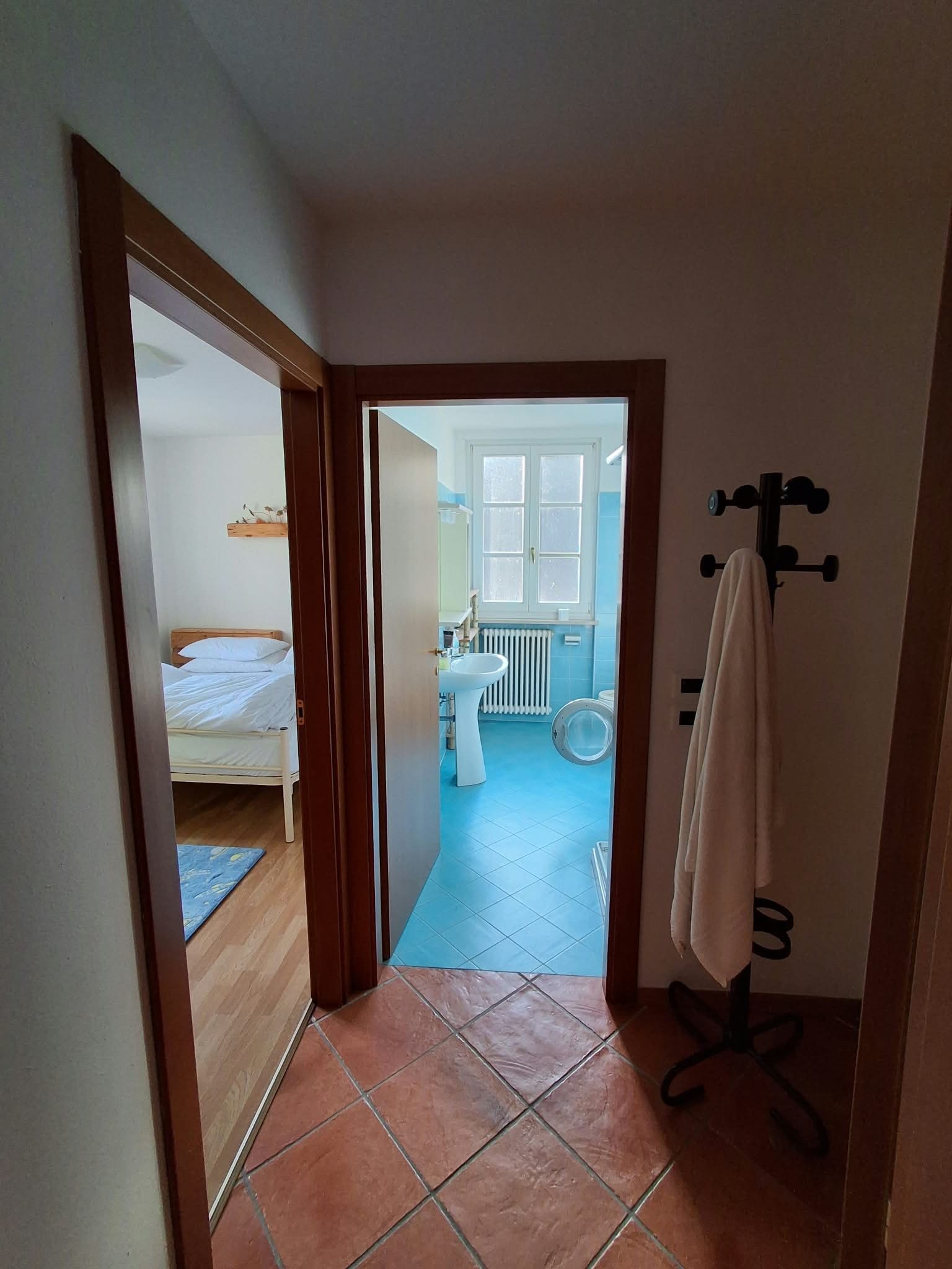 A narrow hallway leading to a bathroom with a blue floor, a white sink, and a towel rack.