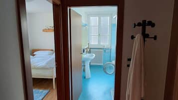 A narrow hallway leading to a bathroom with a blue floor, a white sink, and a towel rack.