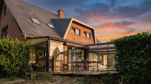 Une maison dotée d’une véranda en verre, d’une façade en briques et d’un toit en pente.