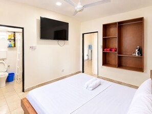 Habitación de hotel con cama, televisión, armario y baño visible a través de una puerta abierta.
