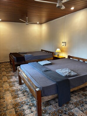 Een kamer met twee bedden, een plafondventilator, een wandlamp en vloertegels met een patroon.