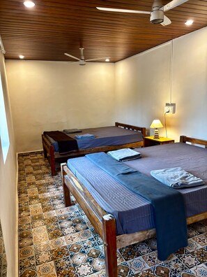 Een kamer met twee bedden, een plafondventilator, een lamp en vloertegels met een patroon.