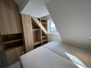 Ein Zimmer mit schrägem Dach, eingebauten Holzregalen, einem Einzelbett und einem Fenster.