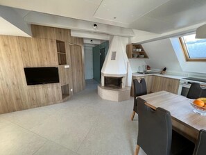 Eine moderne Küche mit eingebautem Herd, ein Essbereich mit Tisch und Stühlen sowie ein an der Wand befestigter Fernseher.