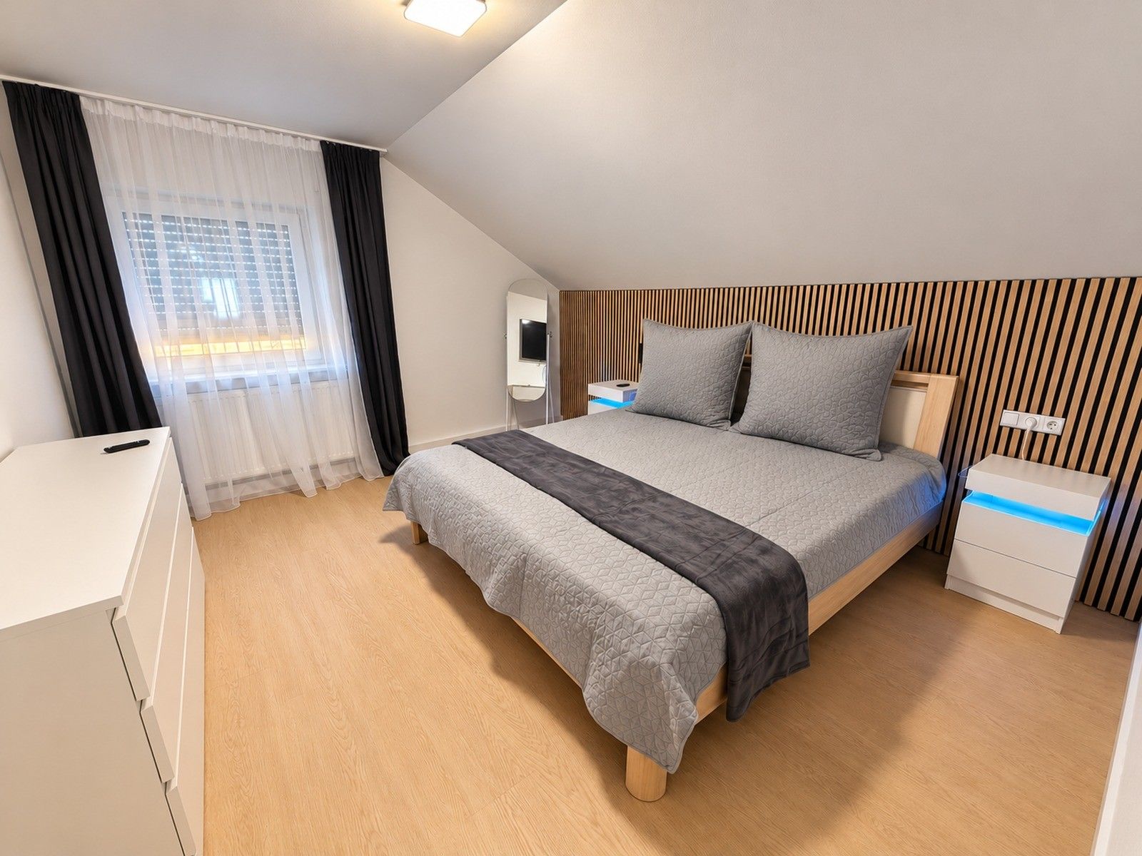 Ein modernes Schlafzimmer mit einem Bett, Nachttischen, einem Spiegel und einem Fenster mit Vorhängen.