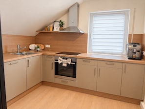 Eine kleine Küche mit integriertem Backofen, einer Kaffeemaschine und einem Fenster mit Jalousien.