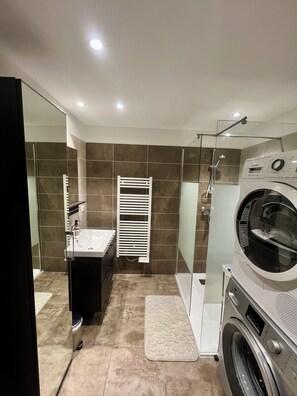 Een moderne badkamer met een glazen douchecabine, een Bosch wasmachine, een wit wastafelmeubel en een handdoekrek.