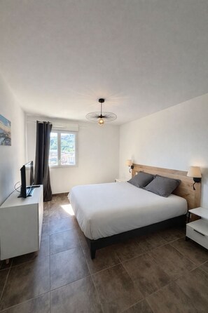 Een slaapkamer met een bed, nachtkastjes, een bureau, een lamp en een raam met gordijnen.