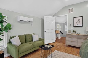 Un salon moderne avec un canapé vert, une petite table d’appoint noire et un plancher en bois.