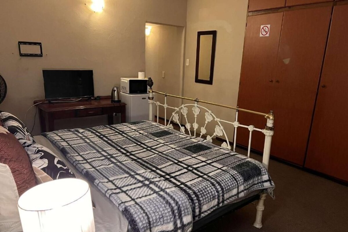 A bedroom with a bed, a desk with a computer, a TV, a lamp, and a wardrobe.